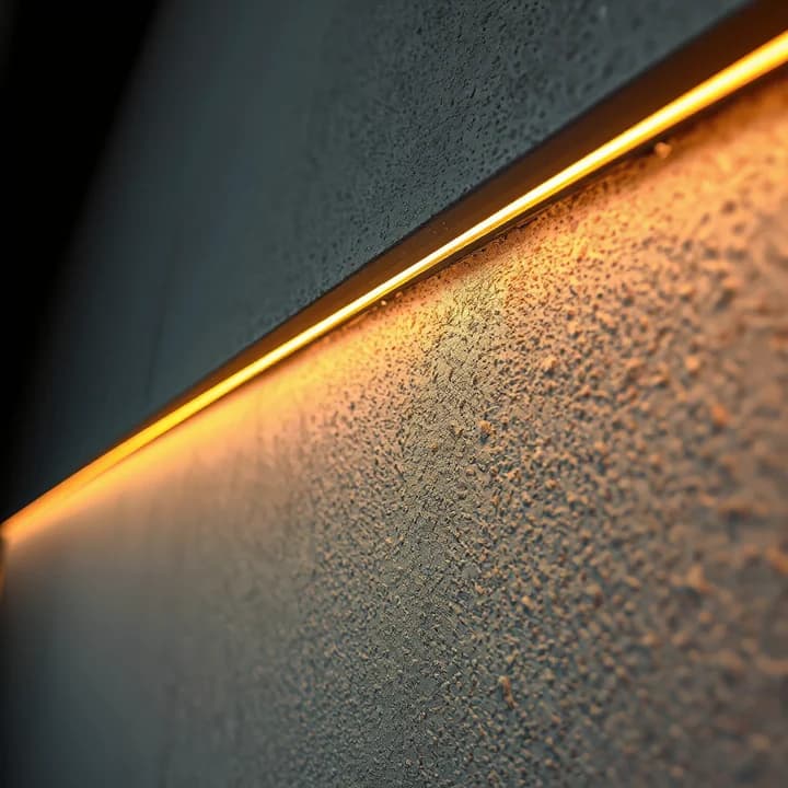 La tira de luz ámbar rasante sobre el estucado grueso de ARENA